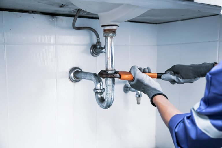 Plumber using a wrench to repair water pipe under the sink